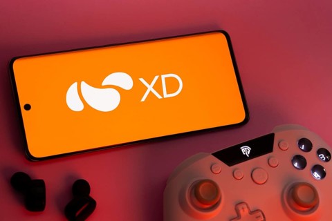 Dhaka, Bangladesh- 22 Mar 2025: Smartphone with XD logo, game controller, and earbuds on a pink