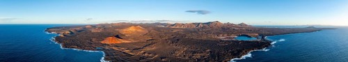 Coast with lava fields, volcanic landscape near Los Hervideros with red volcano Montaña Bermeja, in