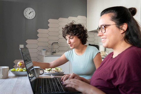 A couple sitting at a kitchen table, enjoying breakfast while working on laptops. They are relaxed