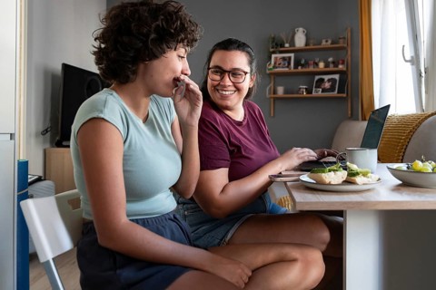 A lesbian couple shares a cozy breakfast in their modern kitchen, with one partner working on a