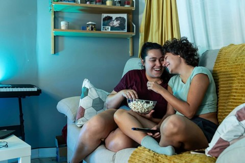 A joyful lesbian couple eating popcorn while watch tv, highlighting domestic harmony and love