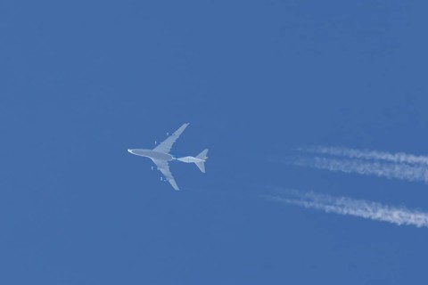 Boeing 747 jumbo jet cargo aircraft flying in a blue sky with contrails or vapour trails behind,