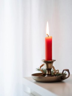 Red candle burning on a brass candlestick decorated with tree branch