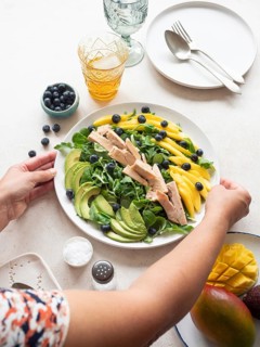 Woman placing a plate of healthy tuna, mango, avocado and blueberry salad on a table