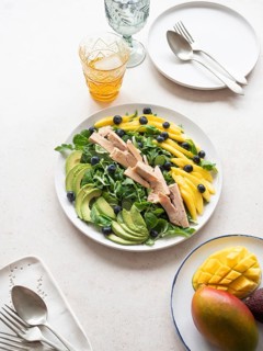 Healthy tuna salad with mango, avocado, blueberries and lamb's lettuce, served on a white plate