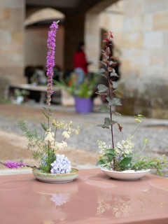 Two beautiful ikebana arrangements stand on a shiny table, reflecting their vibrant colors and