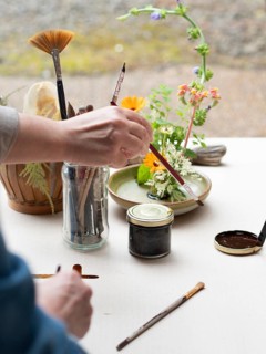 Florist creating ikebana arrangement, painting kenzan and arranging flowers on a table