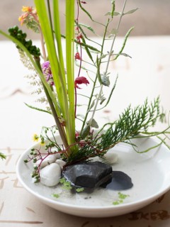 Delicate ikebana flower arrangement in a white bowl with stones and water, showcasing japanese art