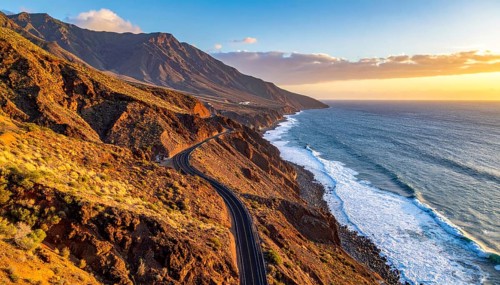Desert landscape converges with ocean along a rugged coastal area, shore break at cliffs, blue