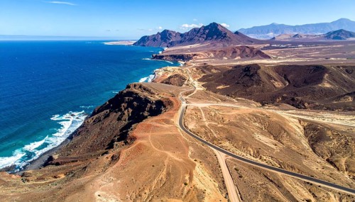 Desert landscape converges with ocean along a rugged coastal area, shore break at cliffs, blue
