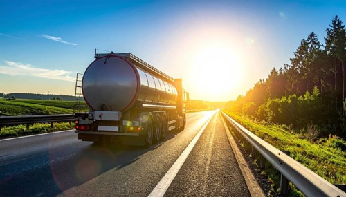 Petrol cargo truck lorry tanker driving on highway hauling oil products at sunrise, wide hilly