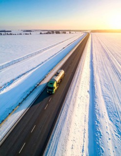 Petrol cargo truck lorry tanker driving on highway hauling oil products at sunrise, wide snowy