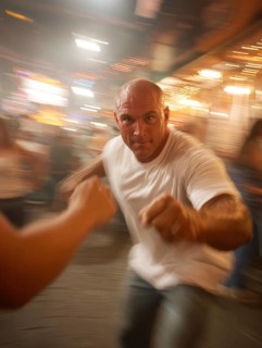 A man gets into a fighting stance, surrounded by dynamic movement and a background filled with