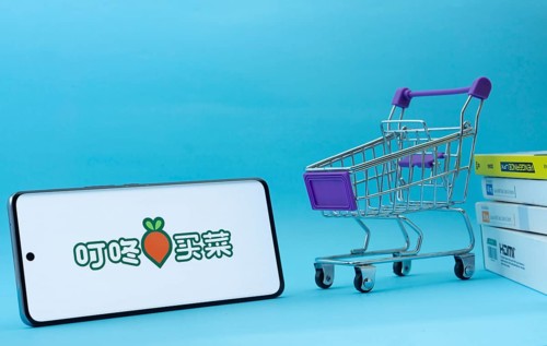 Dhaka, Bangladesh- 03 July 2025: Smartphone with Dingdong Maicai logo next to a small shopping cart