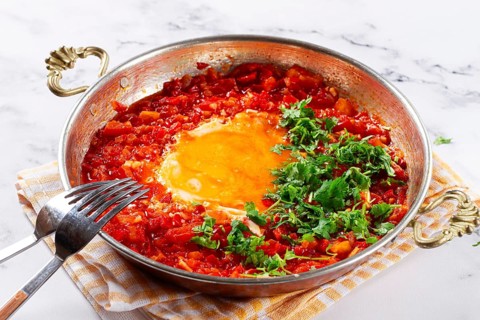 Traditional Turkish dish, scrambled eggs with tomatoes, Menemen, with herbs, in a frying pan,