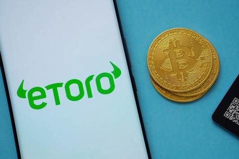 Dhaka, Bangladesh- 22 June 2025: eToro logo on smartphone screen near Bitcoin coin and QR code on