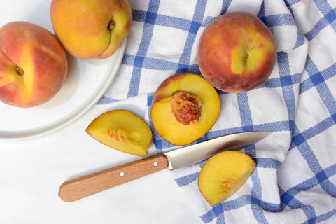 Peach with knife on kitchen towel, peach halves, Prunus persica