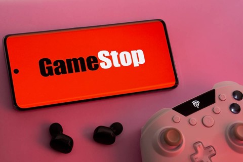 Dhaka, Bangladesh- 15 July 2025: Smartphone with GameStop logo, game controller, and earbuds on a