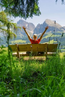 Person on a bench with outstretched arms in front of a mountain landscape, Alpe di Siusi,