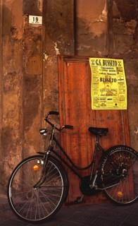 A bike stands in front of an old house wall with a soccer poster of GS Busseto, in honor of