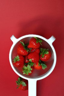 Strawberries in a colander on a red background, Fragaria