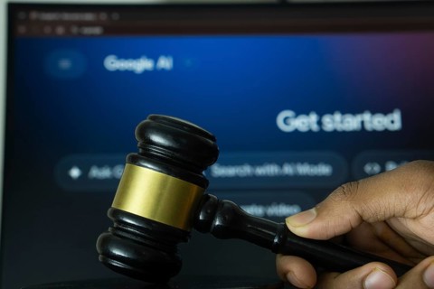 A hand holds a gavel in front of a computer screen displaying Google AI's website