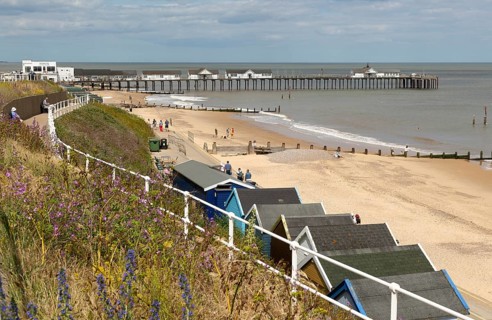 View over beach huts to sandy beach and pier, Southwold, Suffolk, England, UK