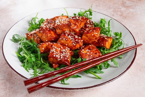 Fried salmon slices, teriyaki with sesame seeds, with arugula salad, top view