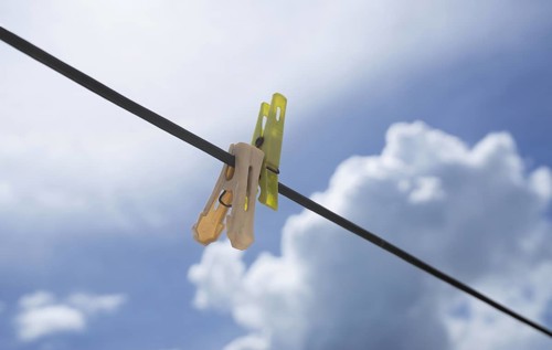 Clothespins on a wire set against a bright blue sky with fluffy clouds