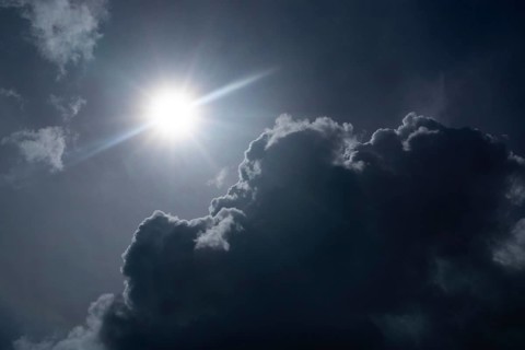 Bright sun shining through dark dramatic clouds against an atmospheric sky