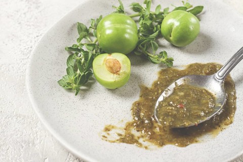 A spoon with tkemali sauce, on a plate, with cherry plum and mint, top view, no people
