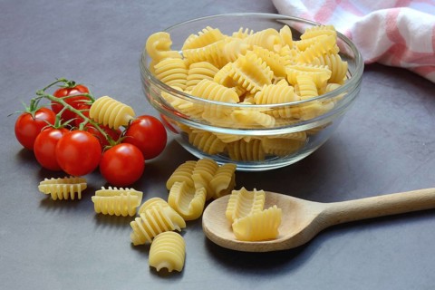 Italian pasta in glass bowl and cooking spoon, Radiatori variety