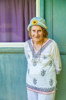 Portrait of a cheerful senior woman wearing a denim hat with a decorative sunflower, standing in