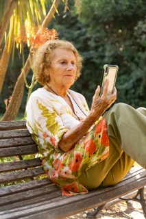 Elderly woman enjoying a tranquil moment in the park, sitting comfortably on a bench while browsing