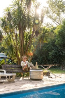 Elderly woman enjoys a peaceful moment in her backyard, sitting on a bench next to a sparkling