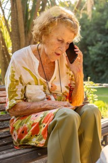 Senior woman sitting on a wooden bench in a serene garden, using her smartphone to enjoy
