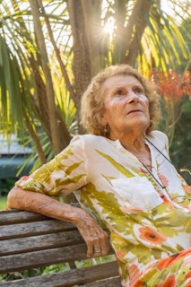 Senior woman enjoying a tranquil moment in a lush garden, sitting on a wooden bench while sunlight