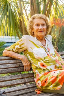Smiling senior woman relaxing on a wooden bench amidst a vibrant tropical garden, soaking in the