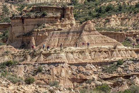 Group of hikers at colorful sandstone rock formations, desert, along gravel road Ruta Jubierre,