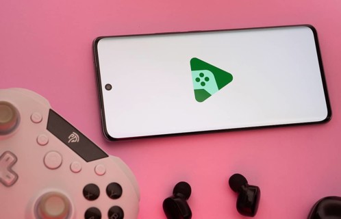 Smartphone with Google Play Games logo, game controller, and earbuds on a pink background
