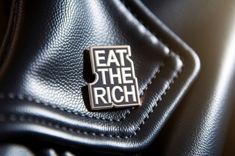 Political protest pin with eat the rich slogan attached to dark fabric symbolizing class struggle