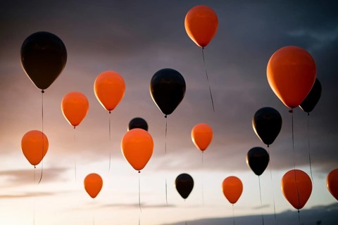 Round orange and black Halloween balloons floating in the sky, festive autumn decoration.