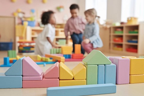 Pastel colored building bricks in sharp focus with children playing in the background, capturing