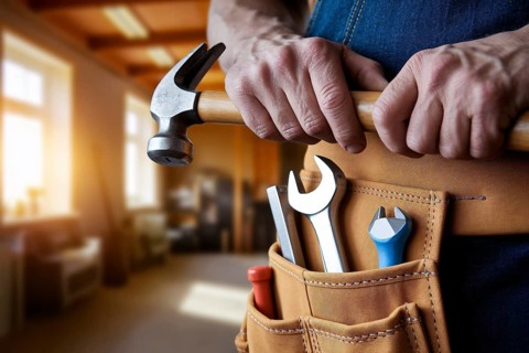Man's tool belt loaded with working tools like wrench, holding a hammer symbolizing traditional