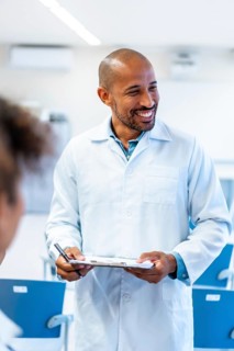Friendly doctor holding a clipboard and smiling while talking with a patient in a hospital room