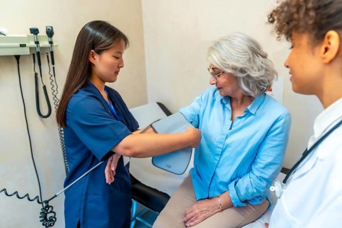 Nurse using sphygmomanometer, taking blood pressure of elderly woman during medical consultation in