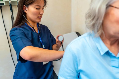 Female doctor using stethoscope examining lungs of senior patient during medical checkup in