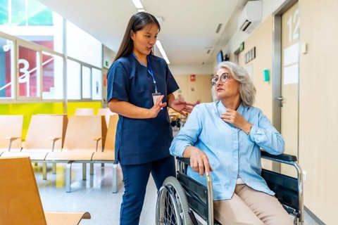 Young nurse assisting and engaging in conversation with senior woman in wheelchair, providing