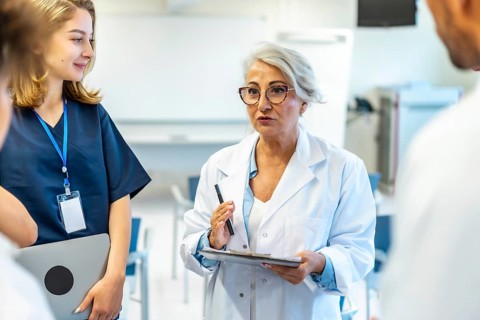 Experienced female doctor leading a medical briefing, holding a clipboard and pen, addressing