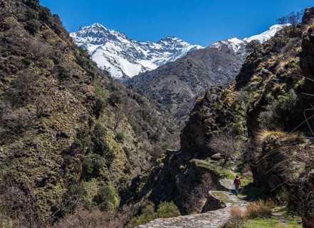 Woman hiking on trail Vereda de la Estrella, snow-covered mountain range in early spring, Sierra